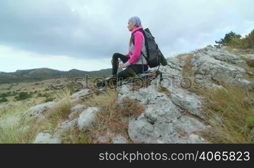 JIB CRANE: Young woman hiking on mountain plateau drinking water sitting on steep cliff looking at the scenic highland Ai-Petri, Crimean mountains