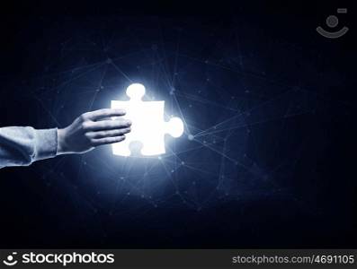 Jigsaw elements in hand. Human hand on dark background holding puzzle glowing element