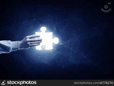 Jigsaw elements in hand. Human hand on dark background holding puzzle glowing element