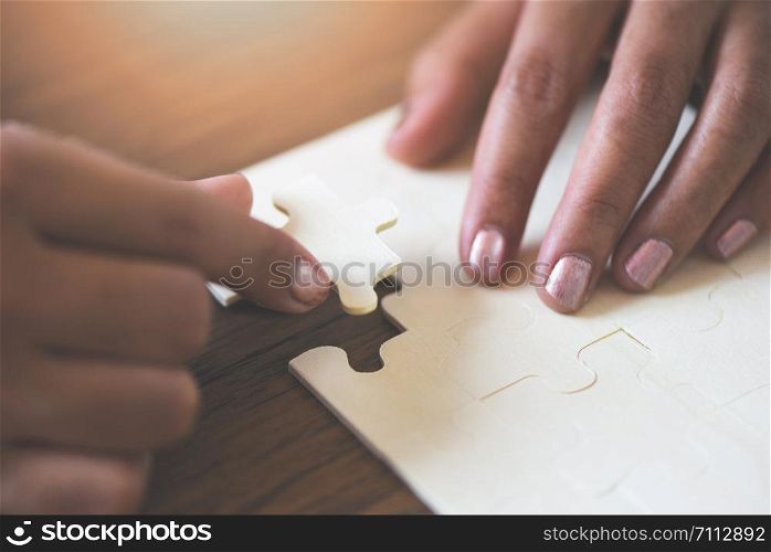 jigsaw puzzle with woman hand connecting jigsaw piece on wooden background / Business solutions partnership success and strategy concept