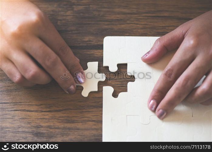 jigsaw puzzle with woman hand connecting jigsaw piece on wooden background / Business solutions partnership success and strategy concept