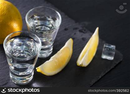 Jin or vodka in glasses with lemon wedges and ice on black background. Alcohol cocktail with citrus and herbs. Copy space