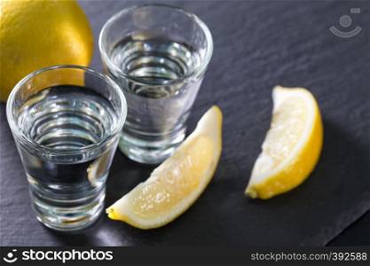 Jin or vodka in glasses with lemon wedges on a black background. Alcohol cocktail with citrus and herbs. Copy space