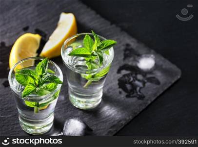 Jin or vodka with mint and ice. Two glasses with a cocktail of mint and ice alcohol with lemons on the black surface. Selective focus. Free space.
