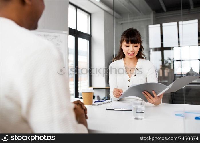 job, business and employment concept - smiling asian female employer or hr manager with folder having interview with male employee at office. employer having interview with employee at office
