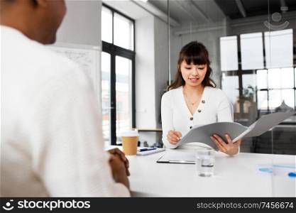 job, business and employment concept - smiling asian female employer or hr manager with folder having interview with male employee at office. employer having interview with employee at office