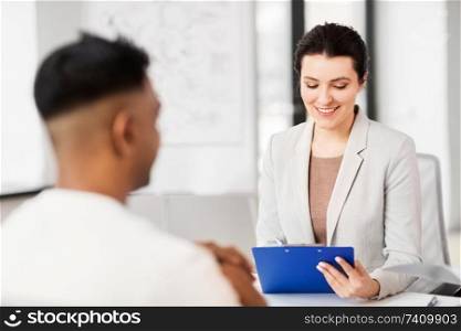 job, business and employment concept - smiling female employer or hr manager with clipboard having interview with male employee at office. employer having interview with employee at office