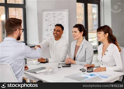 job, hiring and employment concept - international team of recruiters having interview with male employee and shaking hands at office. recruiters having interview with employee