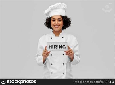 job, work and employment concept - happy smiling female chef in white toque and jacket holding hiring sign over grey background. smiling female chef in toque holding hiring sign