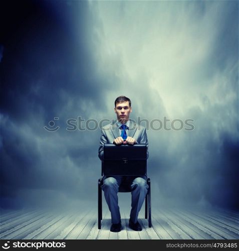 Joblessness. Young businessman sitting on chair with suitcase on knees