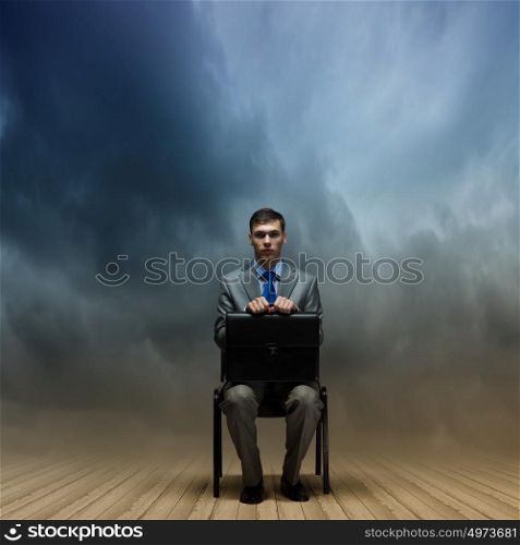 Joblessness. Young businessman sitting on chair with suitcase on knees