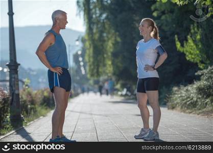 jogging couple check music playlist on phone and plan route before morning running workout with sunrise in the city and sun flare in background
