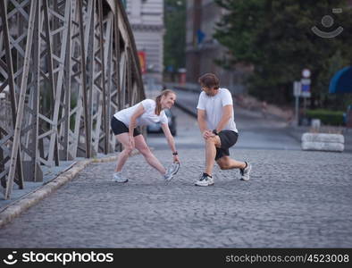 jogging couple warming up and stretching before morning running training workout in the city with sunrise in background