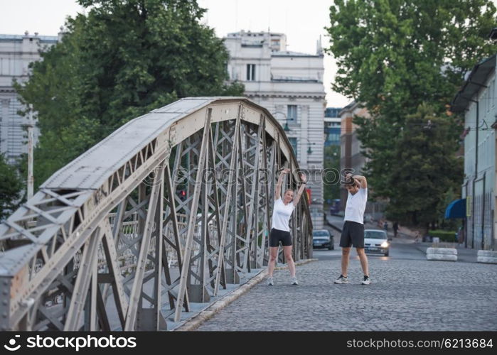 jogging couple warming up and stretching before morning running training workout in the city with sunrise in background