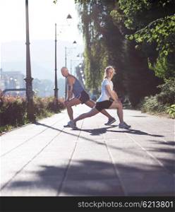 jogging couple warming up and stretching before morning running training workout in the city with sunrise in background
