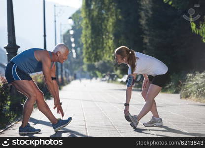 jogging couple warming up and stretching before morning running training workout in the city with sunrise in background