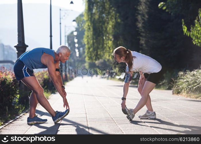 jogging couple warming up and stretching before morning running training workout in the city with sunrise in background