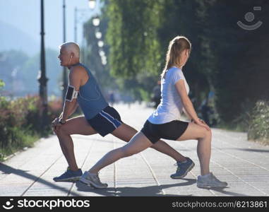 jogging couple warming up and stretching before morning running training workout in the city with sunrise in background