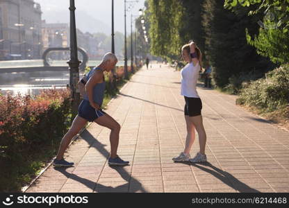 jogging couple warming up and stretching before morning running training workout in the city with sunrise in background