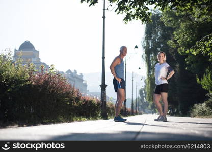 jogging couple warming up and stretching before morning running training workout in the city with sunrise in background