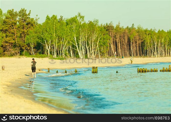 Jogging during summertime, outdoor sports concept. Woman in sportswear running on beach near sea.. Woman in sportswear running through seaside