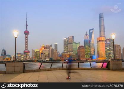 Jogging man in motion blur at city embankment, illuminated Shanghai cityscape in twilight dusk in background, China