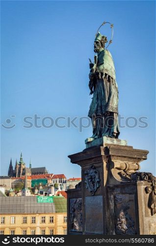 John of Nepomuk (or John Nepomucene) national saint of the Czech Republic statue on Charles Brigde at the site where the saint was thrown into Vltava with St. Vitus Cathedral in background in Prague