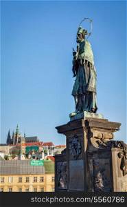 John of Nepomuk (or John Nepomucene) national saint of the Czech Republic statue on Charles Brigde at the site where the saint was thrown into Vltava with St. Vitus Cathedral in background in Prague