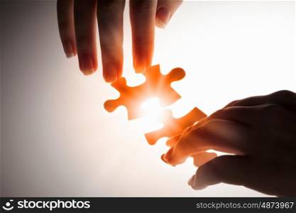Join together. Hand connecting two jigsaw glowing puzzle pieces