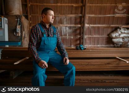 Joiner in uniform at his workplace on timber mill, woodworking machine on background, lumber industry, carpentry. Wood factory, forest sawing in lumberyard. Joiner in uniform at his workplace on timber mill