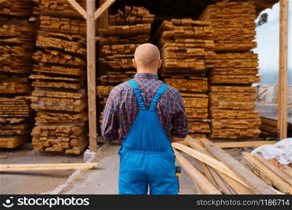 Joiner in uniform check boards on timber mill, lumber industry, carpentry. Wood processing on factory, forest sawing in lumberyard, warehouse outdoor