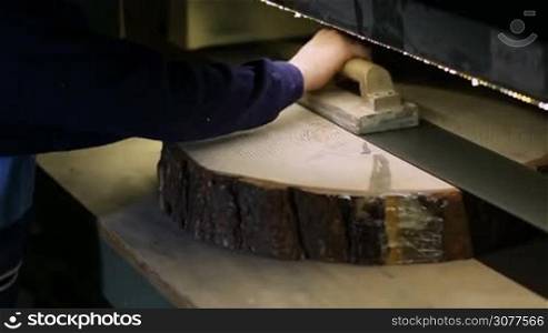 Joinery worker smoothening tree log slice with wood sander machine. Closeup carpenter working with fixed electric belt sander machine and sanding piece of wood in carpentry workshop.