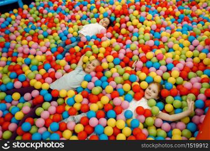 Jouful children lying among many colorful balls in the entertainment center. Girls and boy leisures on holidays, childhood happiness, happy kids on playground. Children lying among many balls, playground