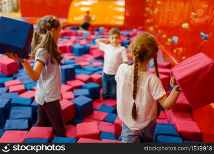 Jouful children plays among soft cubes in the entertainment center. Girls and boy leisures on holidays, childhood happiness, happy kids on playground. Jouful children plays among soft cubes, playground