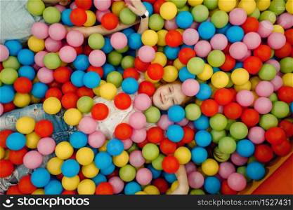 Jouful girl lying among many colorful balls in the entertainment center, top view. Female child leisures on holidays, childhood happiness, happy kids on playground. Girl lying among many colorful balls, playground