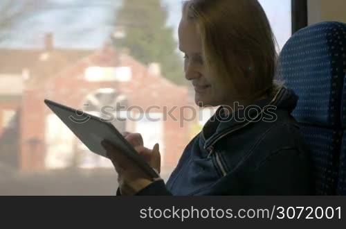 Journey in the train. Young woman using touch pad to communicate while traveling. Entertaining with pad during the trip