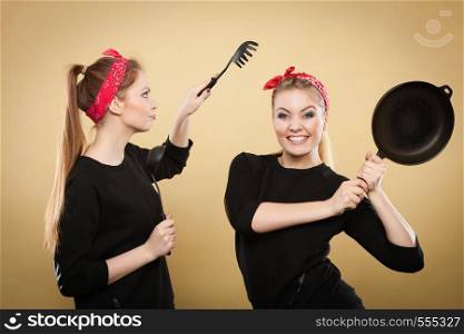 Joy and fun during food preparation. Two blonde smiling women in retro style having fun in kitchen. Playful girls with accessories of cooking.. Retro styled women having fun with kitchen accessories.