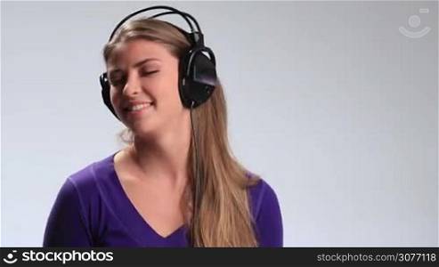 Joy and music. Happy young brunette woman with black earphones fooling around while listening to music on white background. Smiling girl enjoying music, expressing her cheerful mood in the rhythm of music with funny facial expressions and gestures.
