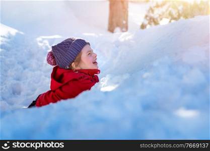 Joyful child in the snow, cute cheerful little girl lying down in the pile of snow and laughing, enjoying winter holidays, happy carefree childhood 