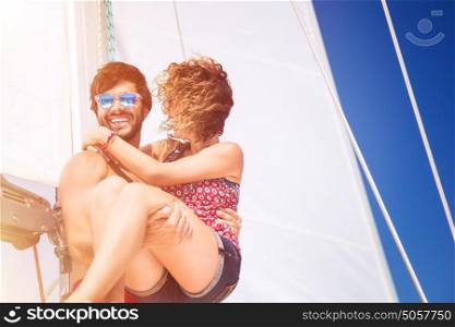 Joyful couple on sailboat, handsome man carrying on hands his lovely girlfriend, spending honeymoon vacation in the sea, active summer time vacation