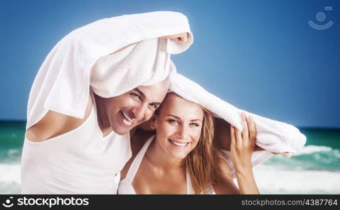 Joyful couple on the beach, happy enamored woman and man peeking from the towel, having fun on tropical resort, with pleasure spending honeymoon &#xA;