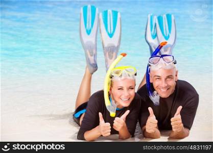 Joyful diver couple lying down on the beach, wearing mask and flippers for snorkeling, gesturing by hands good mood, active summer time vacation