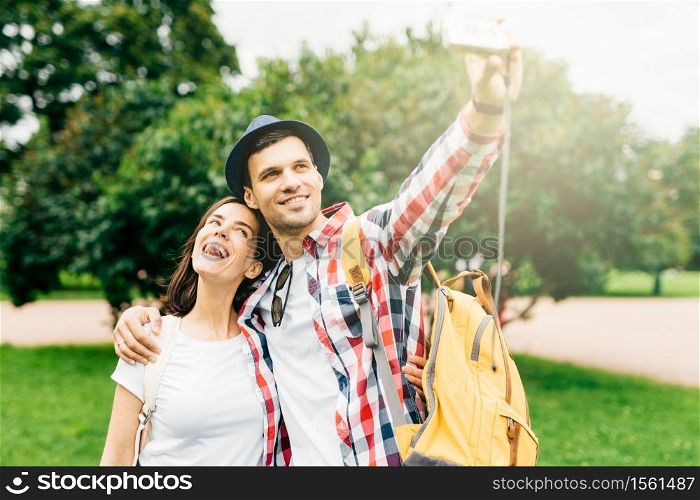 Joyful female and her best friend having excursion in park, making selfie, having happy expressions while hugging. Female and male walking on street. Positive emotions, facial expressions concept