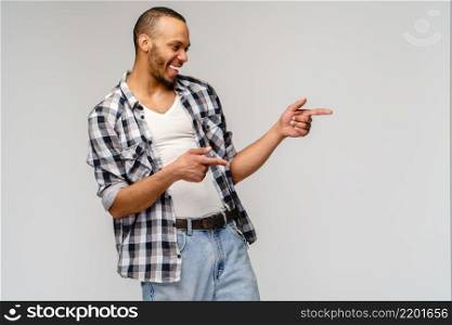 Joyful friendly african-american young man iwearing casual shirt pointing by finger at empty copy space.. Joyful friendly african-american young man iwearing casual shirt pointing by finger at empty copy space