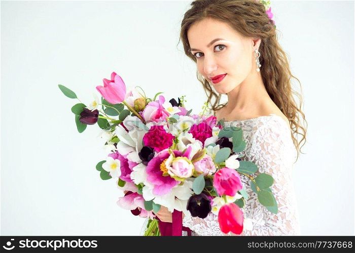 joyful girl bride in a white knitted dress posing with a bouquet of flowers in the studio on a white background