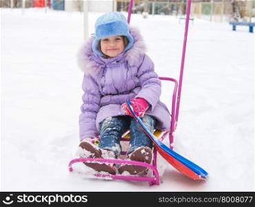 Joyful girl sitting on a sled in the snowy weather. disheveled and happy five year old girl sitting on a sled