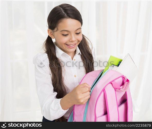 joyful hispanic schoolgirl zipping up school bag