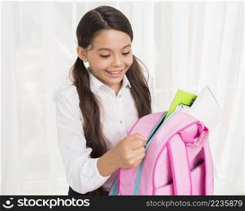 joyful hispanic schoolgirl zipping up school bag