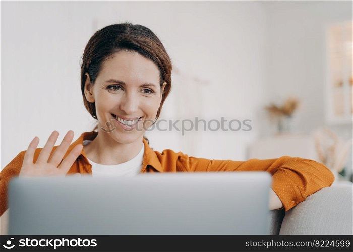 Joyful hispanic woman answer video call on laptop waving hand hello. Positive smiling latina female makes welcome gesture, greeting friend, chatting online using computer webcam. Pleasant conversation. Smiling hispanic woman chatting online by video call on laptop waving hand hello, greeting friend