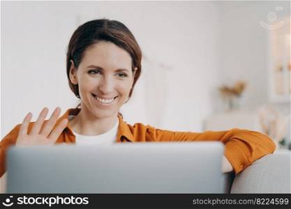 Joyful hispanic woman answer video call on laptop waving hand hello. Positive smiling latina female makes welcome gesture, greeting friend, chatting online using computer webcam. Pleasant conversation. Smiling hispanic woman chatting online by video call on laptop waving hand hello, greeting friend